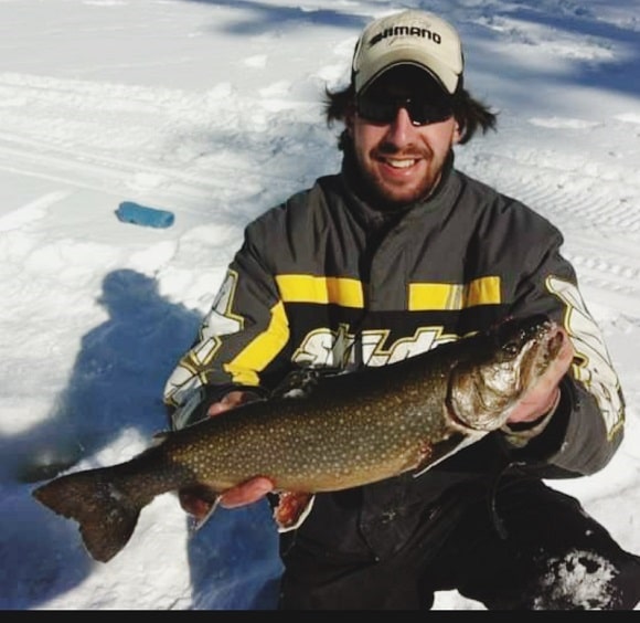 an ice angler on a frozen lake holding a big splake that he has caught on a lipless crankbait