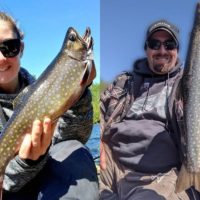 two anglers on a boat holding a beautiful brook trout and a splake