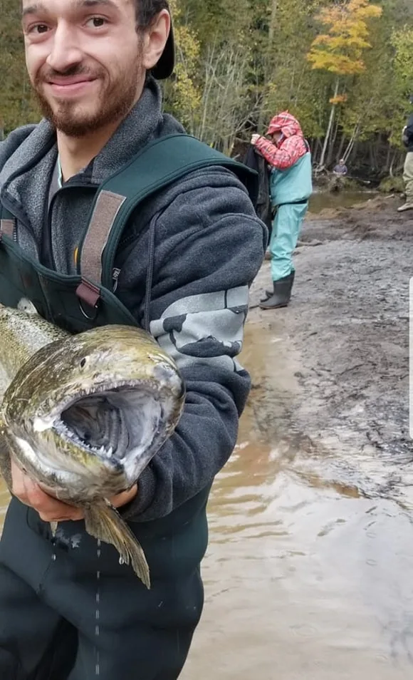 a happy fisherman on a river bank holding a giant king salmon showing its many teeth