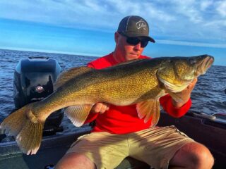 a fisherman on his boat holding a really big walleye that he has caught jigging