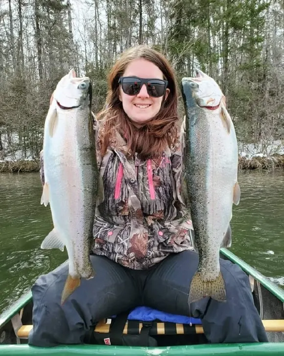 a female angler in a boat holding a pair of silvery rainbow trout caught in a lake