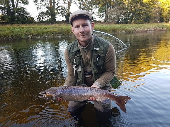 a fly fisherman on a river holding a dark atlantic salmon that he has caught on a streamer