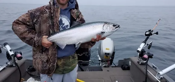 a fisherman on his boat holding a silver chinook salmon 