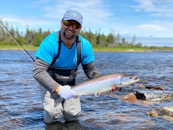 a fly fisherman on a river with a beautiful silvery atlantic salmon