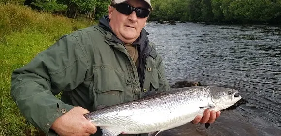 an angler on a river holding a beautiful silver Atlantic salmon 