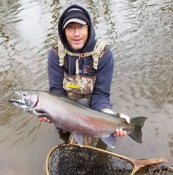 an angler on a river bank holding a giant steelhead trout