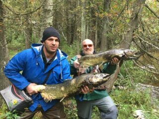 two anglers on a river bank each holding a big zombie salmon