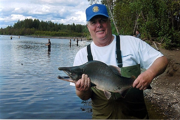 a happy angler on a river holding a small pink salmon that he has caught on a dry fly