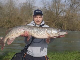a predator angler holding a big pike that he has caught on a murky river