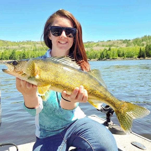 a female angler on a boat holding a big walleye that she has caught on a slow trolled crankbait