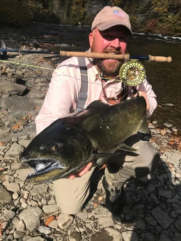 a fisherman on a river holding a big chinook salmon