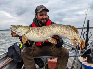 a predator angler on his boat holding a giant northern pike