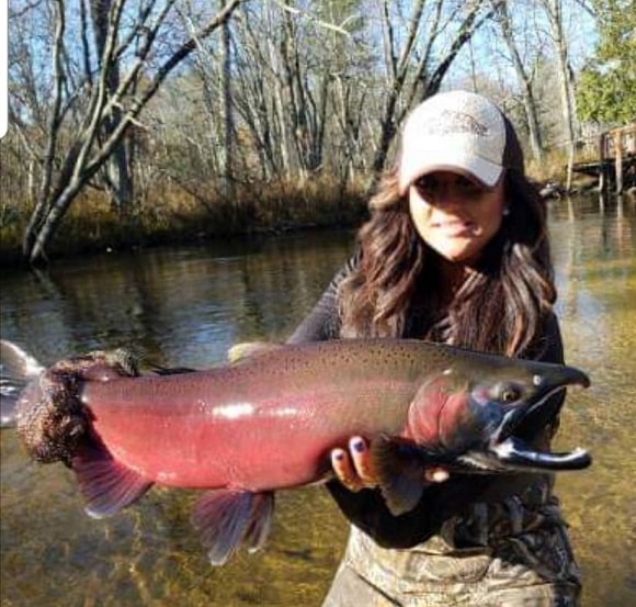 a female angler on a river holding a big coho salmon