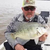 a crappie angler on his boat holding a really big stained water crappie