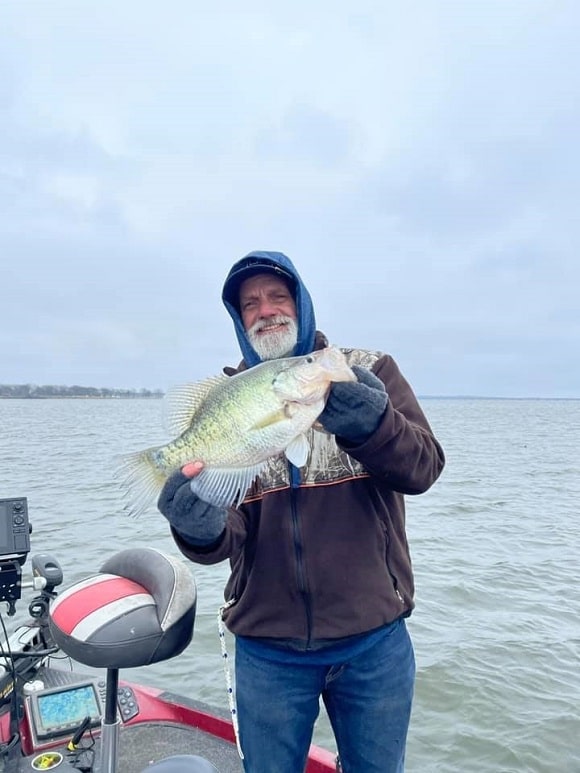 a happy angler on a lake with a very big stained water crappie