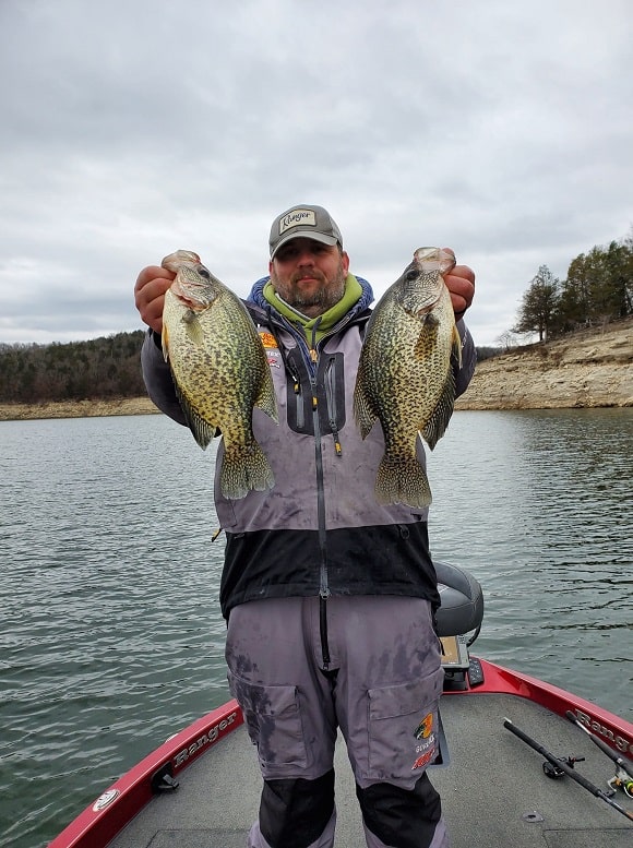 a fisherman on his boat holding two nice crappie caught in murky water