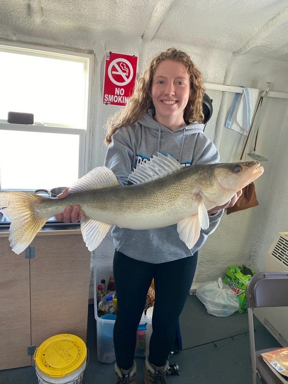 an ice angler in a fish house on lake of the woods holding a huge walleye