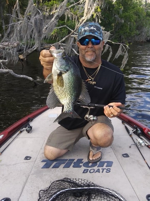 a happy angler on his boat holding a huge crappie that he has caught near a structure
