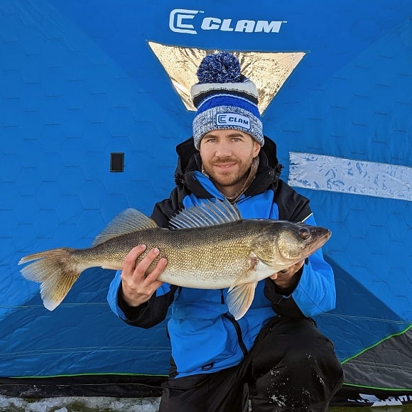 an ince angler in front of his poå-up shelter on Mille Lacs holding a fat walleye