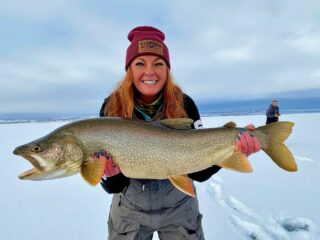 a female ice angler on a frozen lake holding a giant lake trout