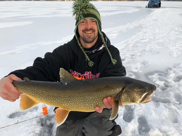 an ice angler holding a nice lake trout that he has caught on a jig 