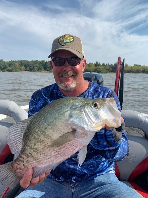 a happy angler on his boat holding a huge female post-spawn crappie