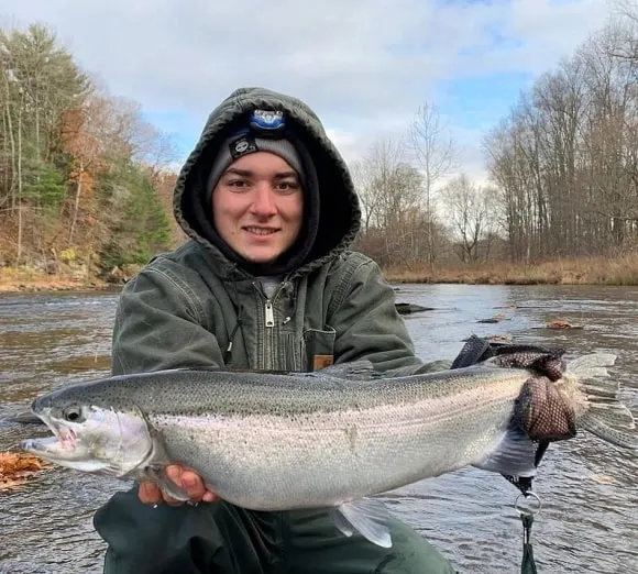 a young trout angler on a river with a big steelhead that he has caught on a rainy day