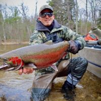 a trout angler on a river bank with a big and beautiful steelhead