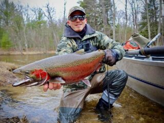a trout angler on a river bank with a big and beautiful steelhead