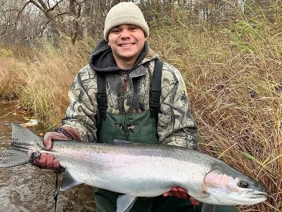 a new york angler on a river holding a really big steelhead