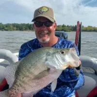 a happy angler on his boat holding a huge female post-spawn crappie