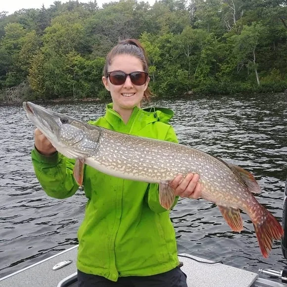 a female angler on a boat holding a nice northern pike