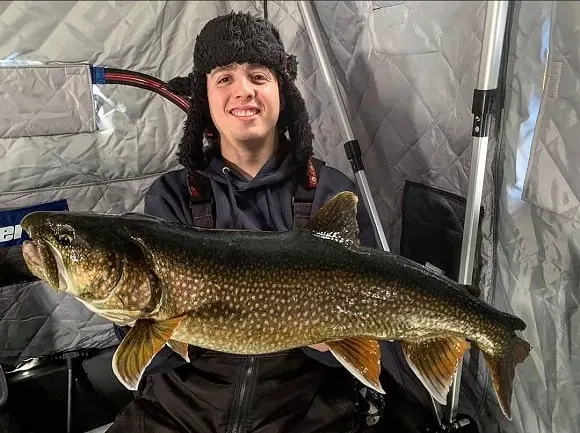 a happy ice angler in his shelter holding a nice lake trout