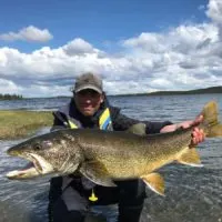 a trout angler in front of a big lake holding a beautiful lake trout
