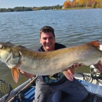 a predator angler on his boat holding a giant musky that he has caught on a live sucker