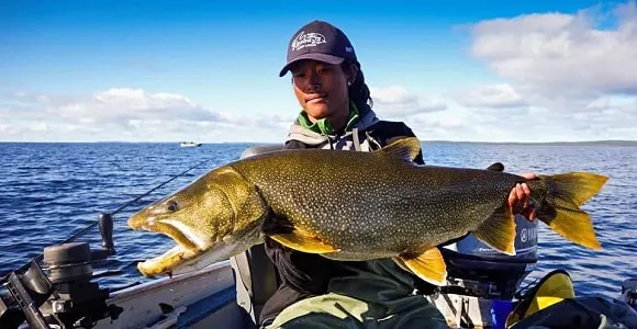 a female trout angler on a lake with a really nice lake trout
