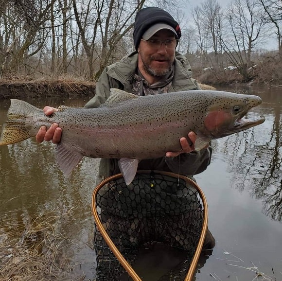 a trout angler on a river with a giant steelhead