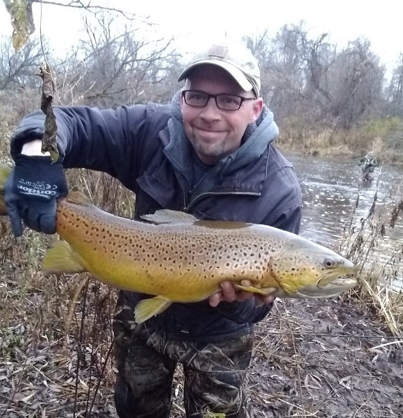 a trout angler in front of a tributary with a giant brown trout