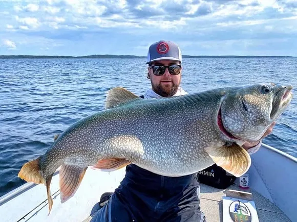 as happy fisher on his boat holding a huge lake trout