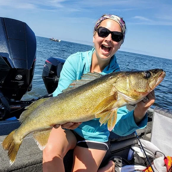 a happy female angler on a boat holding a trophy-sized walleye