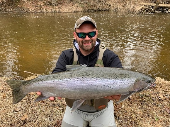 a happy trout angler on a river holding a really big steelhead