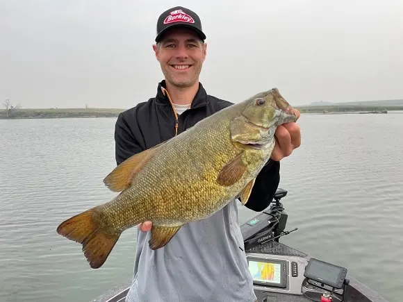 a fisher on a boat holding a big smallmouth bass caught in May