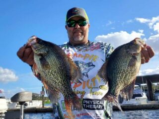 a crappie angler on his boat holding two gaint slabs