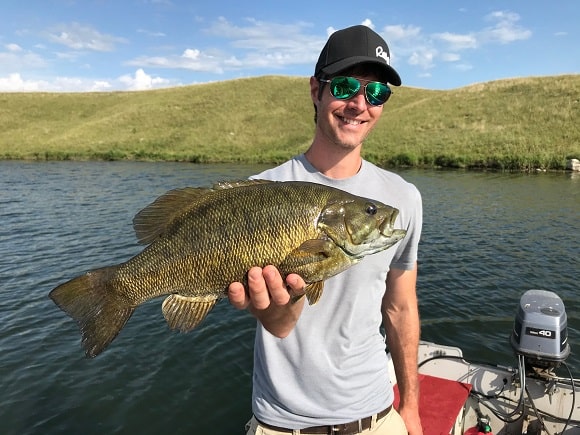 a bass angler on a lake holding a pre-spawn male smallmouth bass