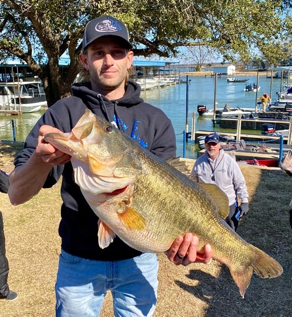 a bass angler near a lake holding a gigantic female largemouth bass