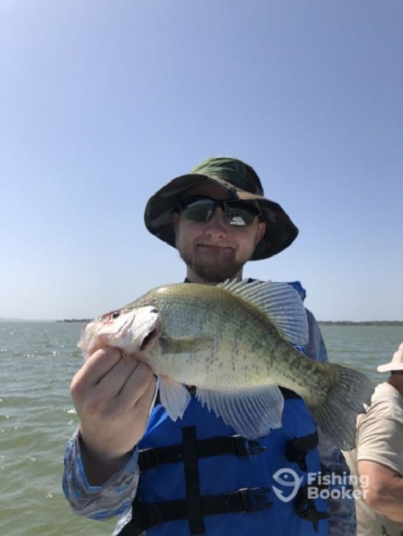 an angler on a fishing boat holding a big crappie caught in February in Florida