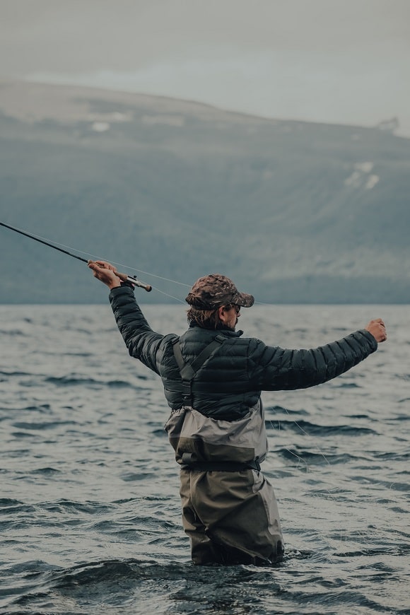 a fly fisherman casting out his rod in a lake