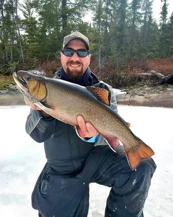 an ice fisherman on a frozen lake holding a huge brook trout