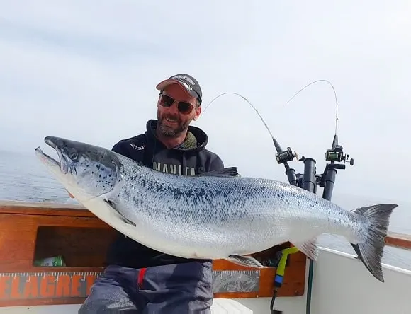 a european trolling angler on his boat holding a giant atlantic salmon