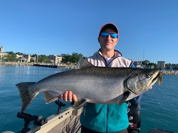 a happy angler on a boat on Lake Michigan holding a big fall king salmon